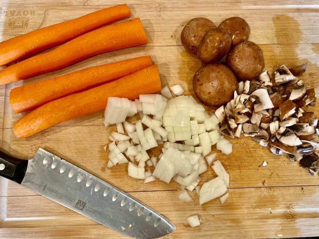 Chopping carrots onions, and mushrooms on a wooden cutting board