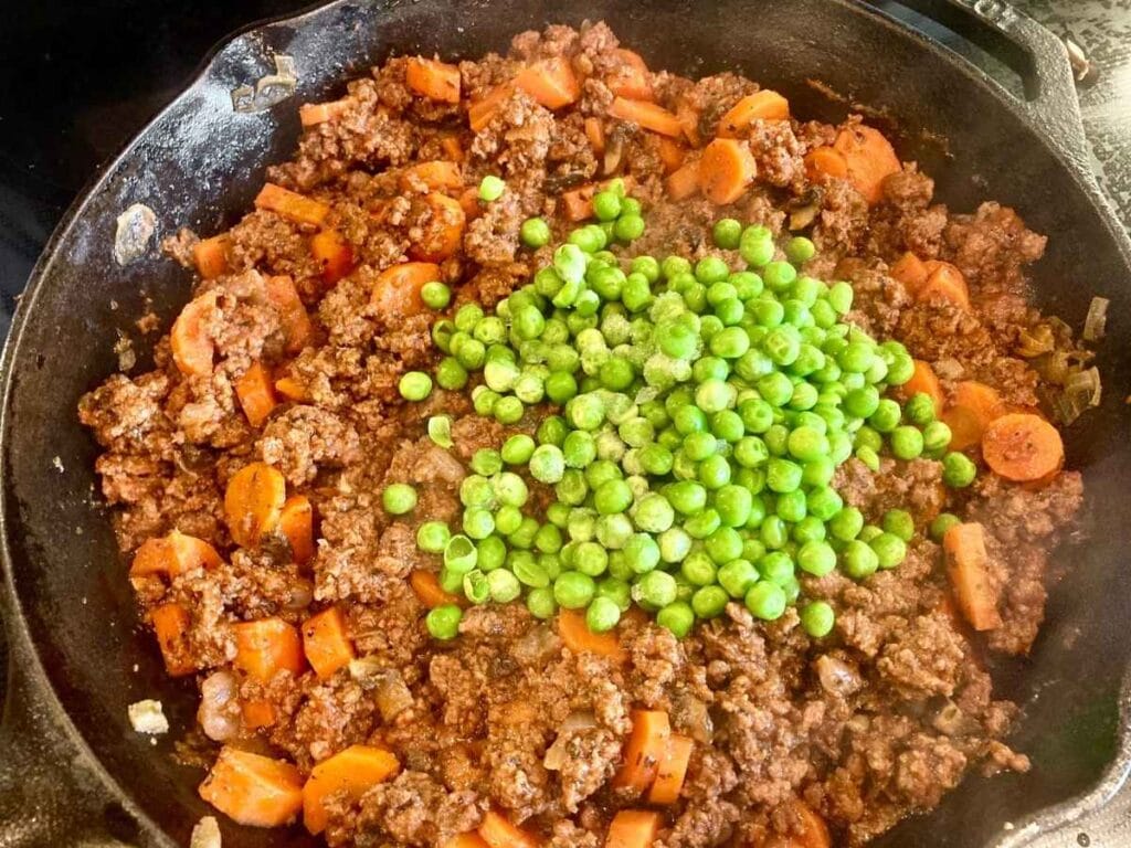 Adding peas to ground beef and vegetable mixture