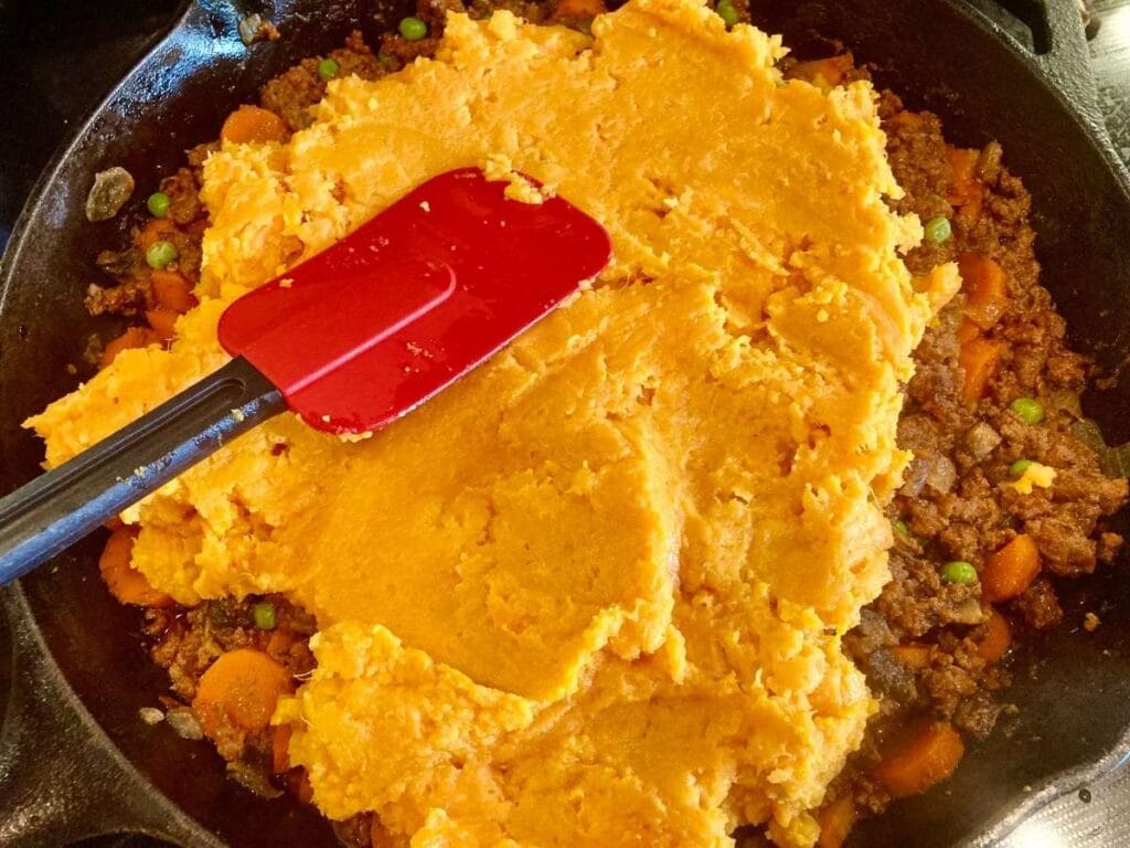 Spreading mashed sweet potatoes over cottage pie