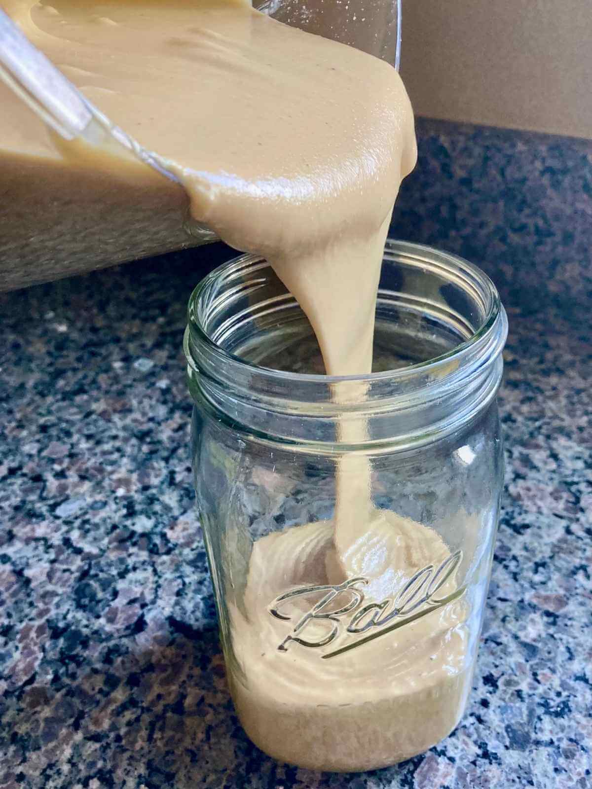 Pouring cashew butter from a food processor into mason jar.