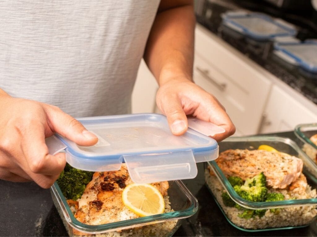 Man placing lid on glass food storage container filled with leftovers.