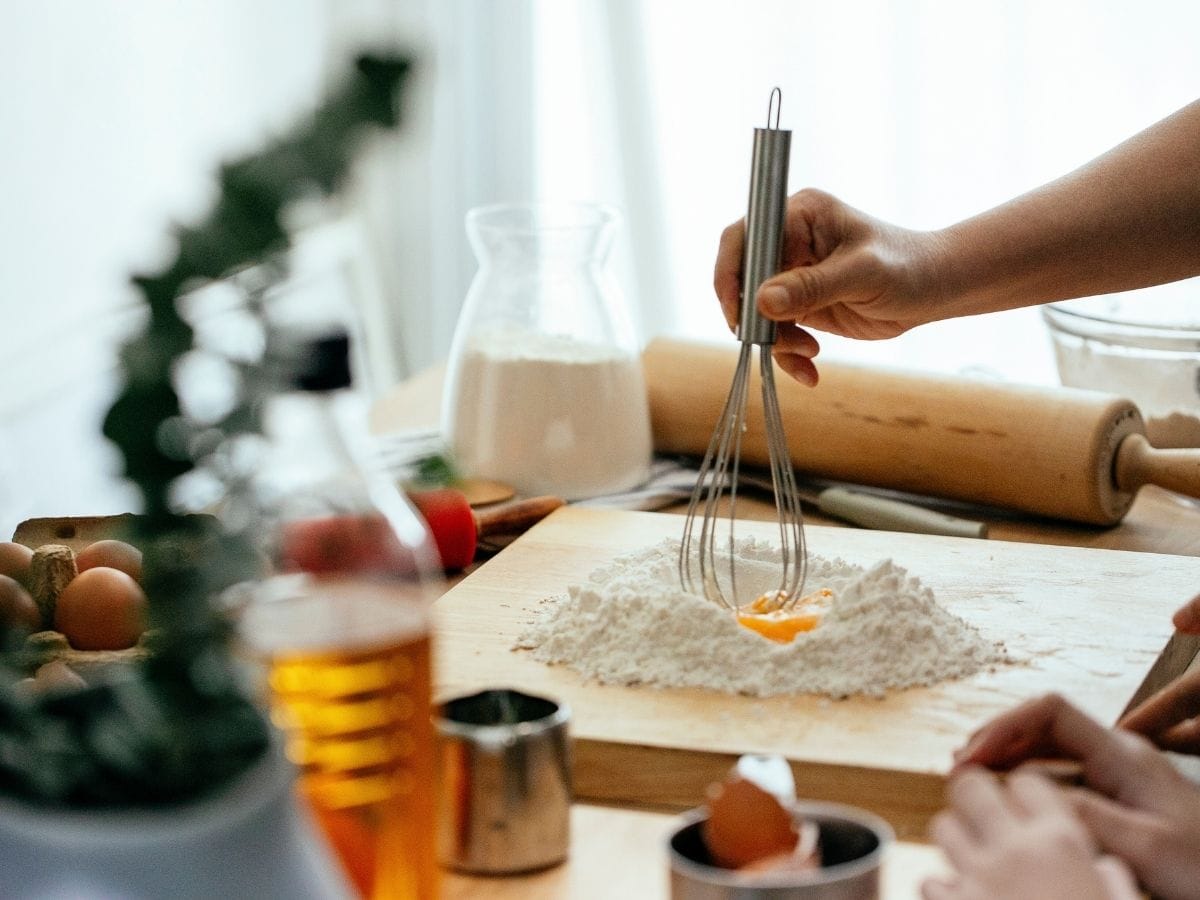 Hands whisking egg into flour on a wooden cutting board.