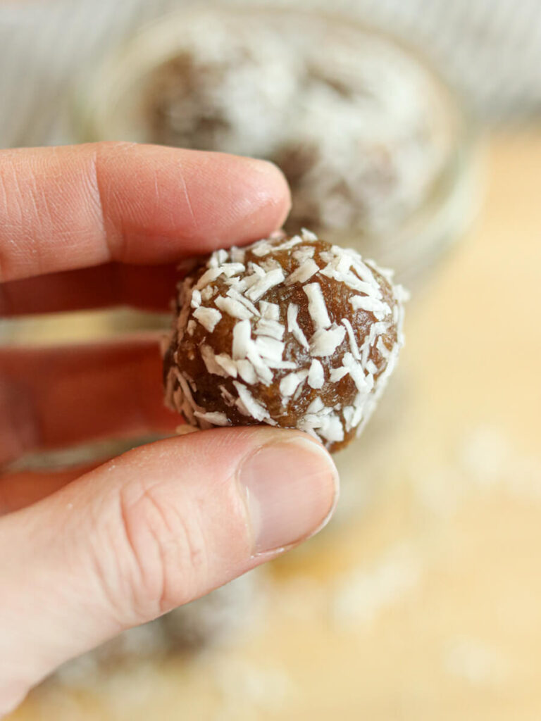 Holding an energy ball rolled in coconut between someone's fingers.