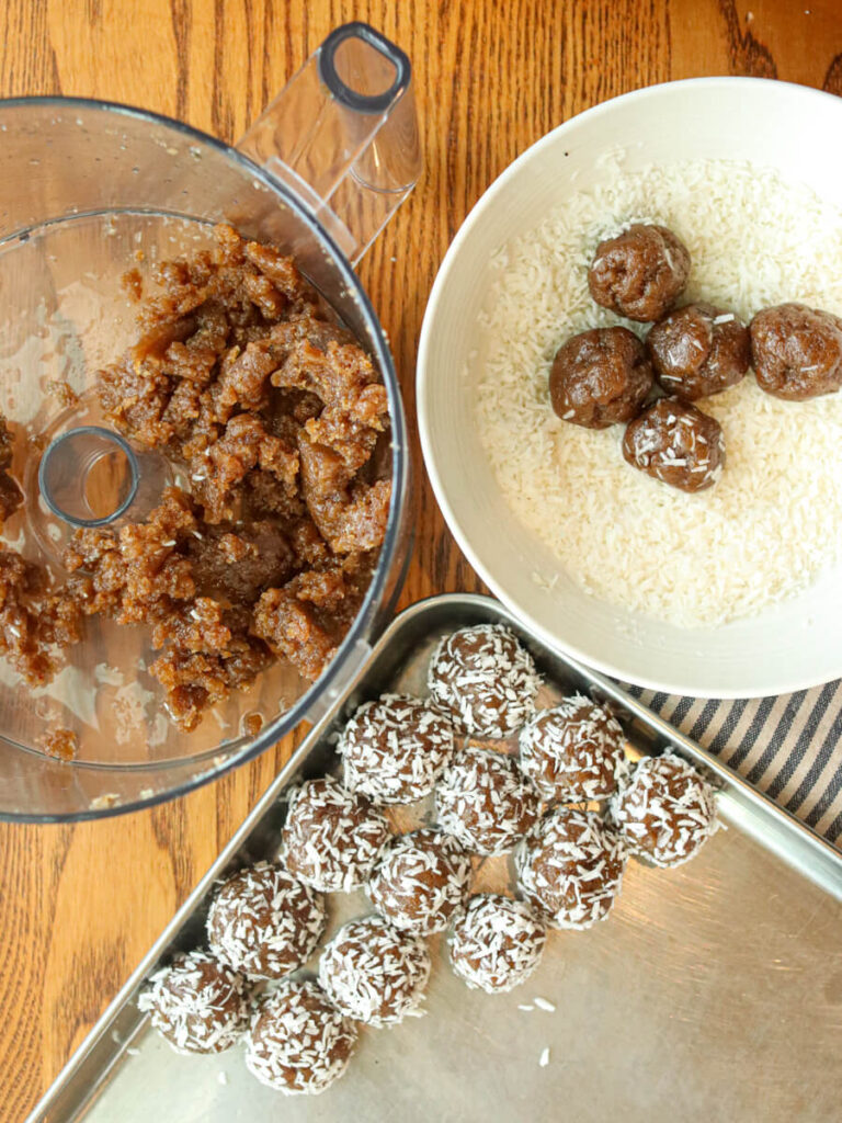 Rolling energy balls in coconut and placing them on a baking sheet.