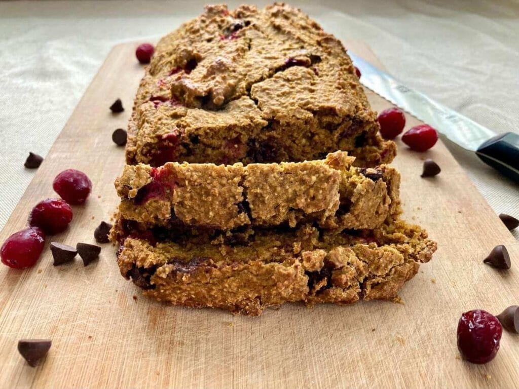 Pumpkin cranberry bread on a cutting board with a few slices cut into it.
