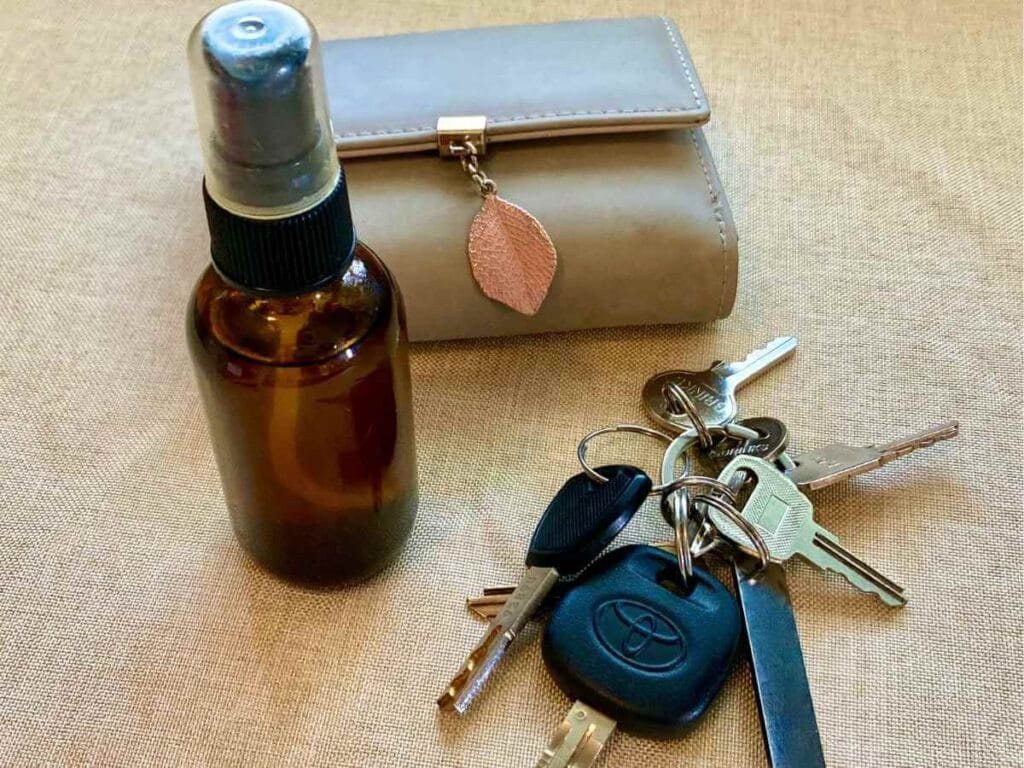 Glass bottle of hand sanitizer spray with keys and a wallet.