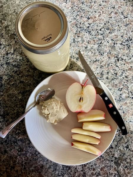 Mason jar with cashew butter beside a plate with a sliced apple and scoop of cashew butter