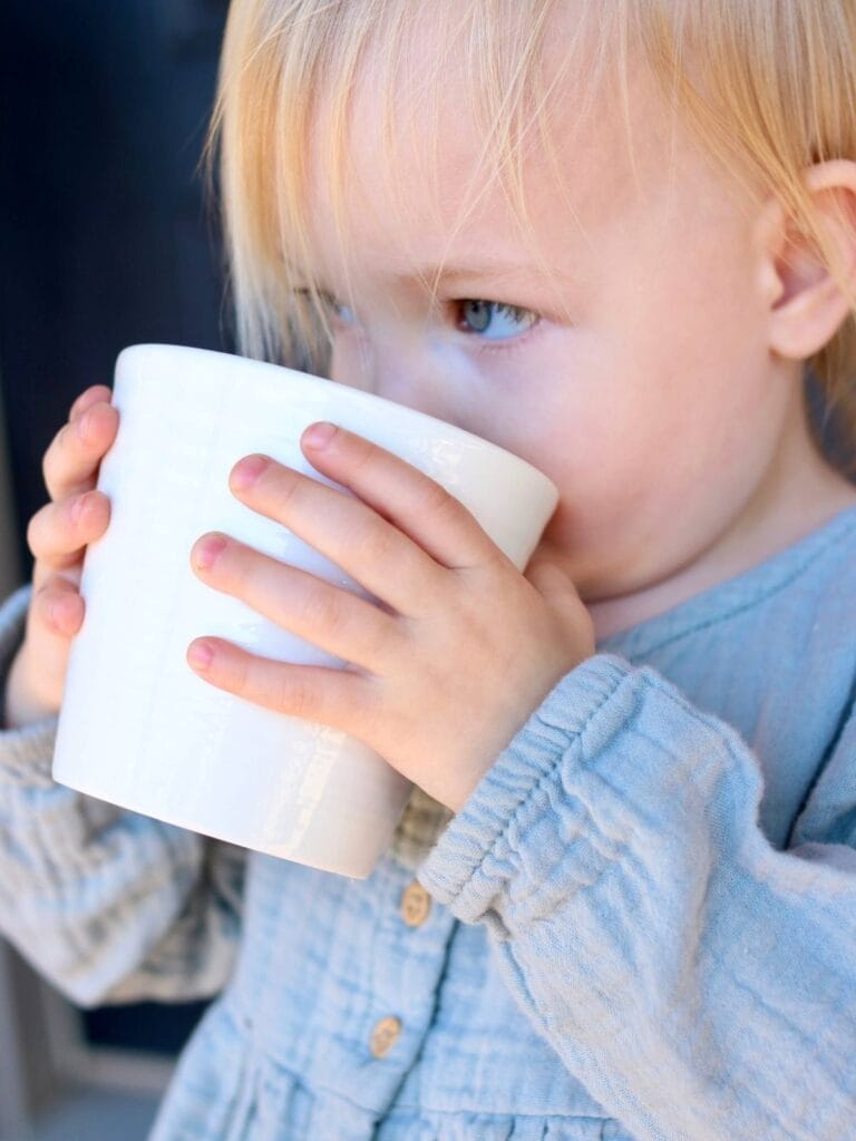 Toddler drinking bone broth from a mug.