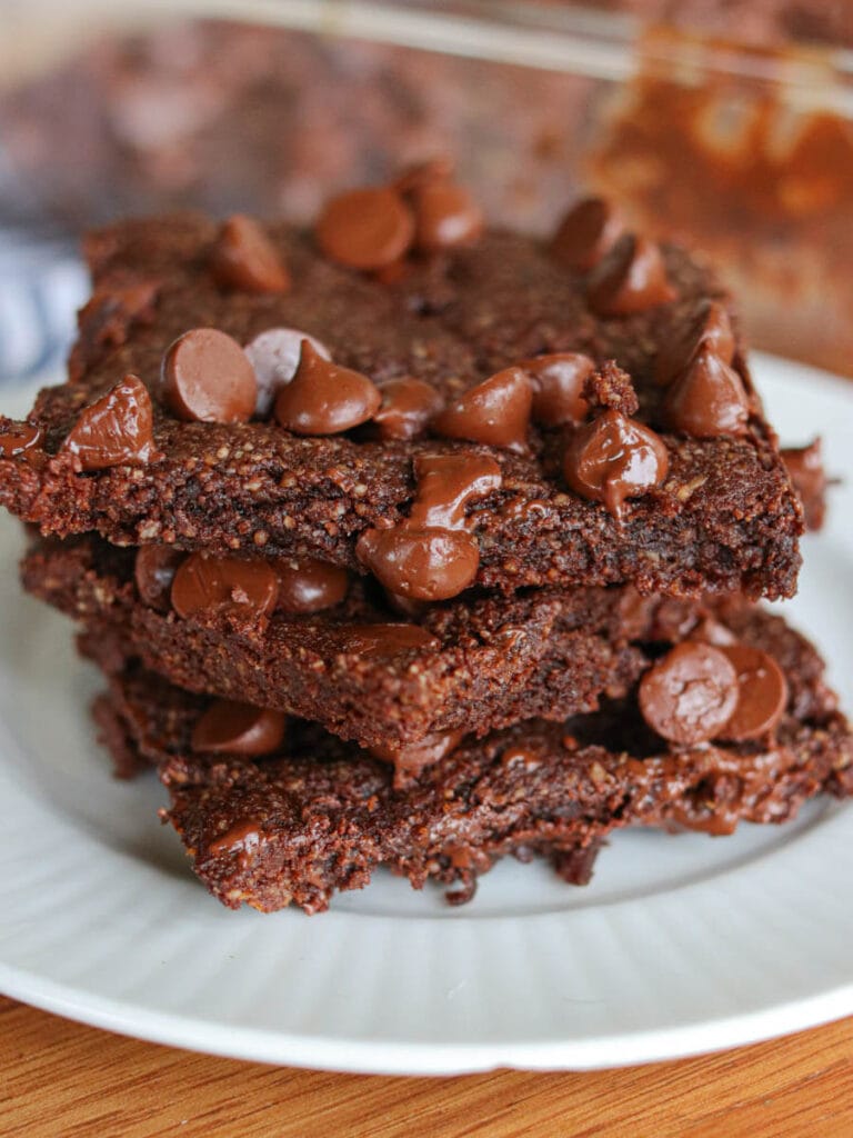 Stack of three vegan almond flour brownies with chocolate chips on a white plate.
