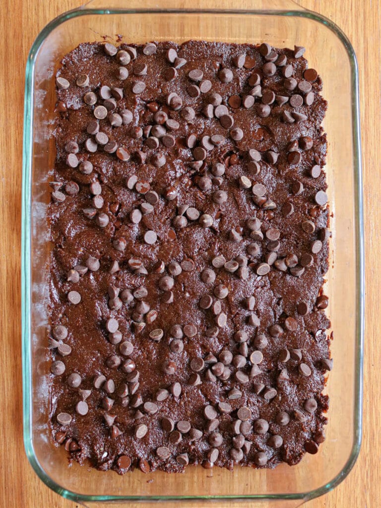 A glass pan of vegan brownie batter with chocolate chips on top ready to be baked.