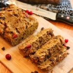 Close-up view of a partially sliced loaf of gluten-free pumpkin bread on a cutting board.