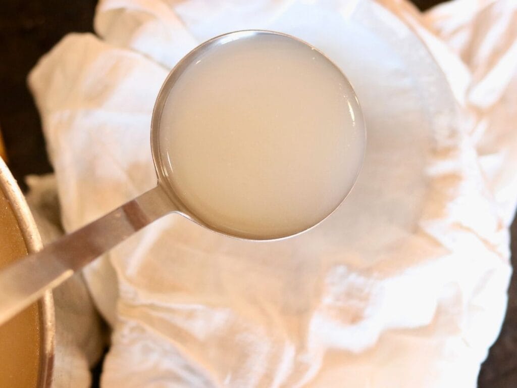 Ladle full of bone broth over a cheesecloth.