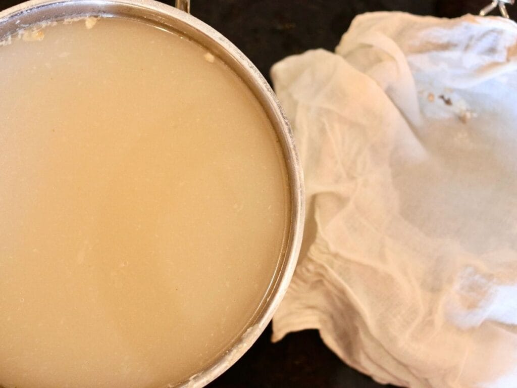 Pot of warm broth next to a cheesecloth over a strainer.