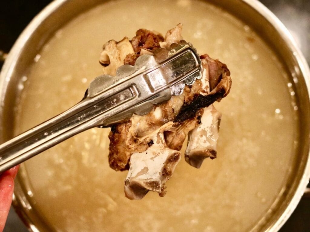 Using tongs to pull beef bones out of bone broth.