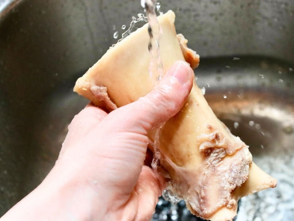 Hand rinsing beef bone under stream of water.