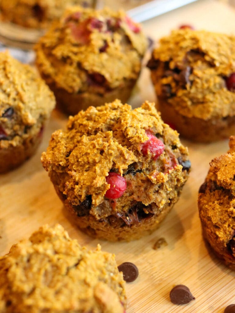 Close-up of a gluten-free pumpkin cranberry muffin on a cutting board with other muffins.