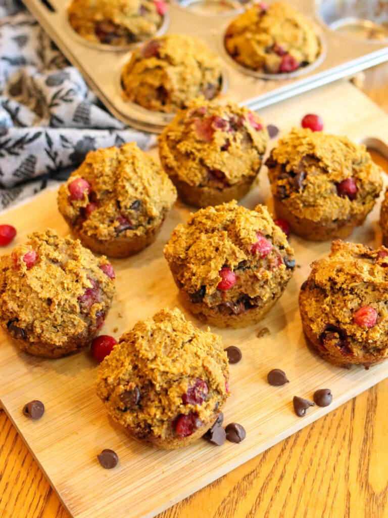 Healthy pumpkin muffins on a cutting board with a pan with more muffins in the background.