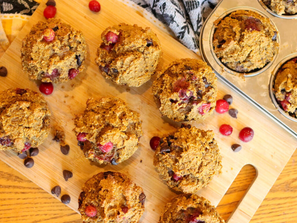 Gluten-free pumpkin cranberry muffins on a cutting board surrounded by chocolate chips and cranberries.
