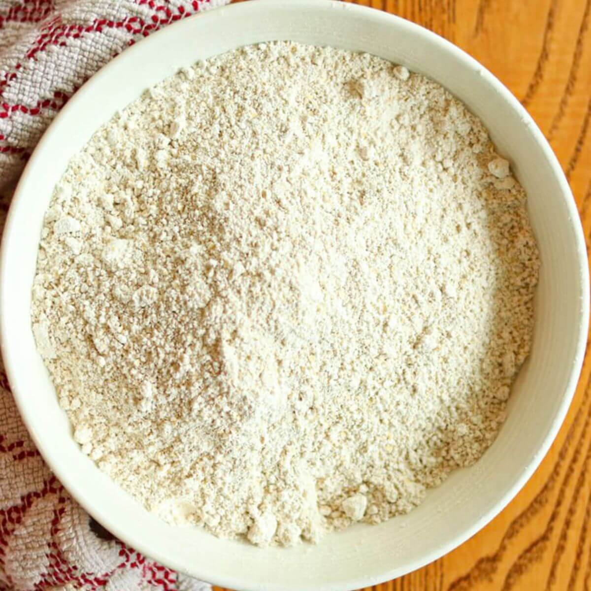 A closeup view of a white bowl full of oat flour that has been ground at home.