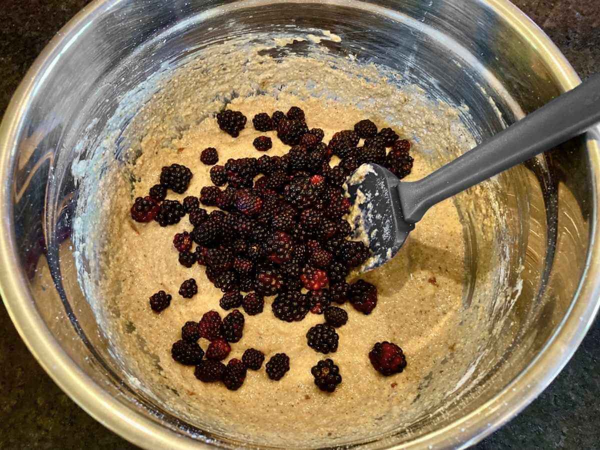 Folding blackberries into batter in a bowl.