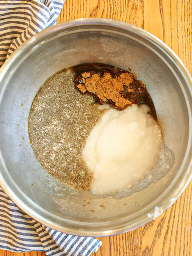Coconut oil, sugar, chia eggs, and other wet ingredients in a bowl on a table.