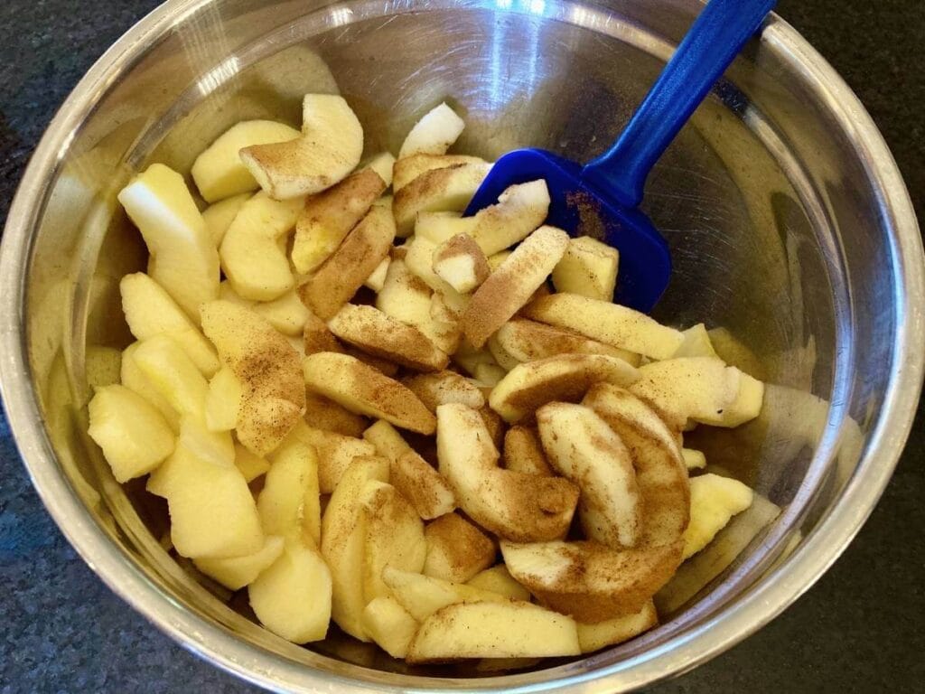 Mixing spices with apple slices in a bowl.