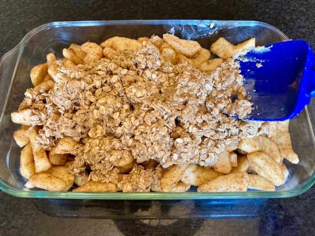 Spreading oat mixture over apples in a baking pan.