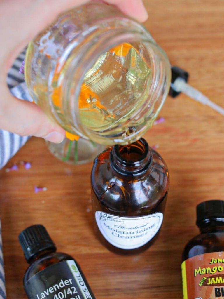 Pouring Castile soap into an amber glass spray bottle on a wooden surface.