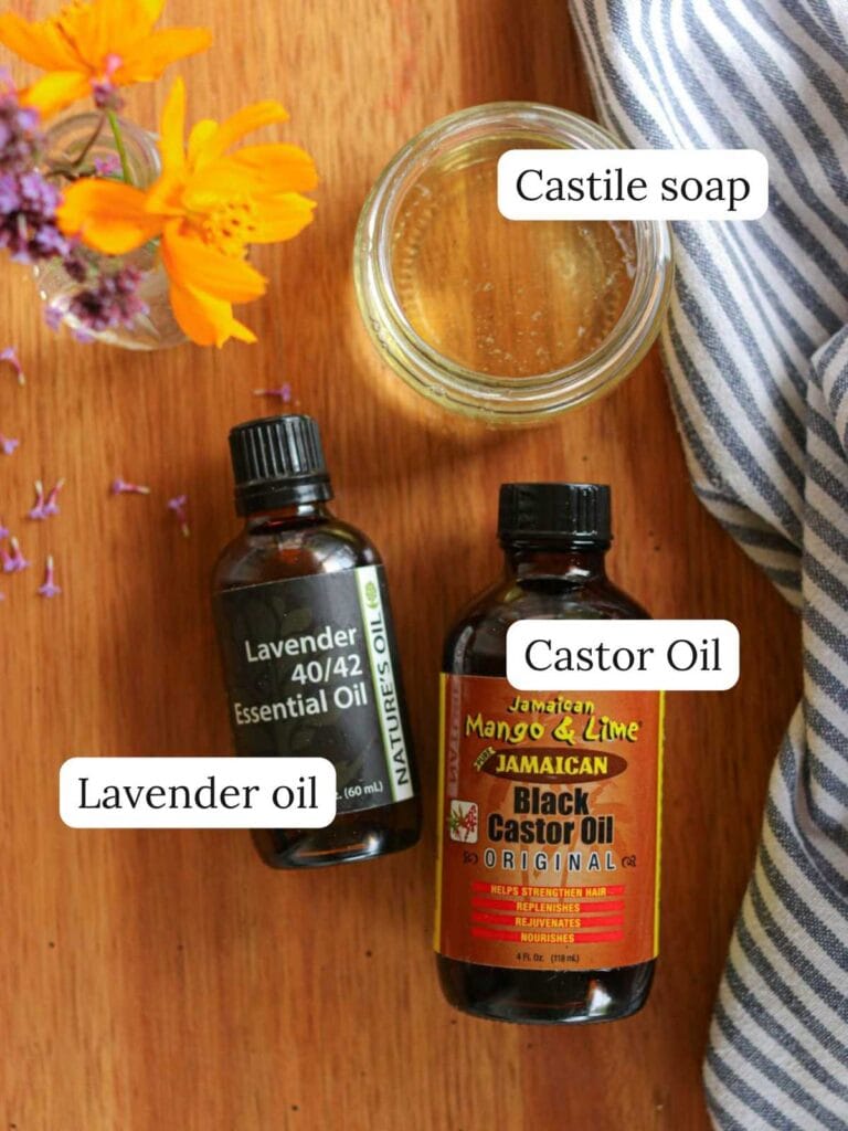 Ingredients on a wooden table including lavender oil, castor oil, and Castile soap.