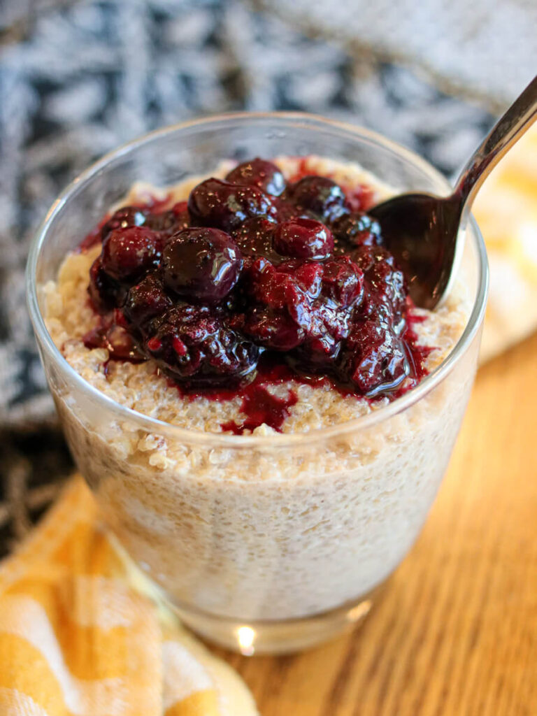 A spoon in a glass of quinoa pudding and fruit sauce.