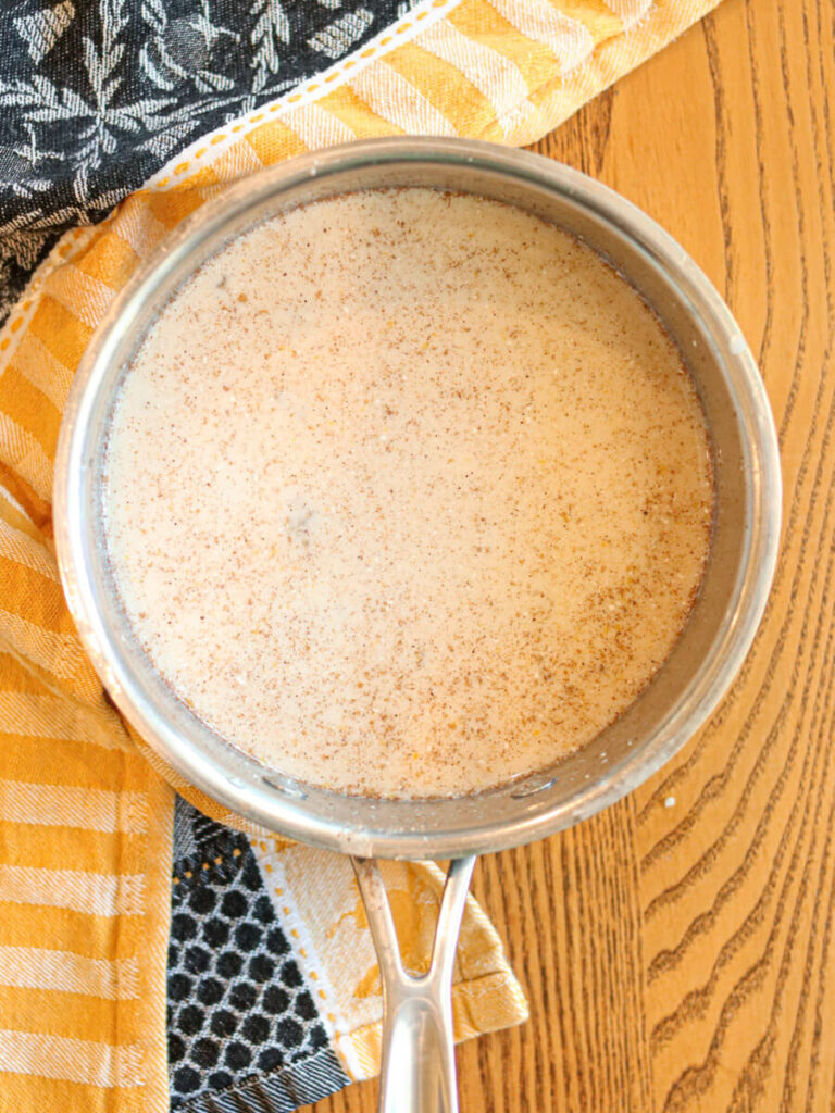 Quinoa stirred into milk mixture in a pan on a table.