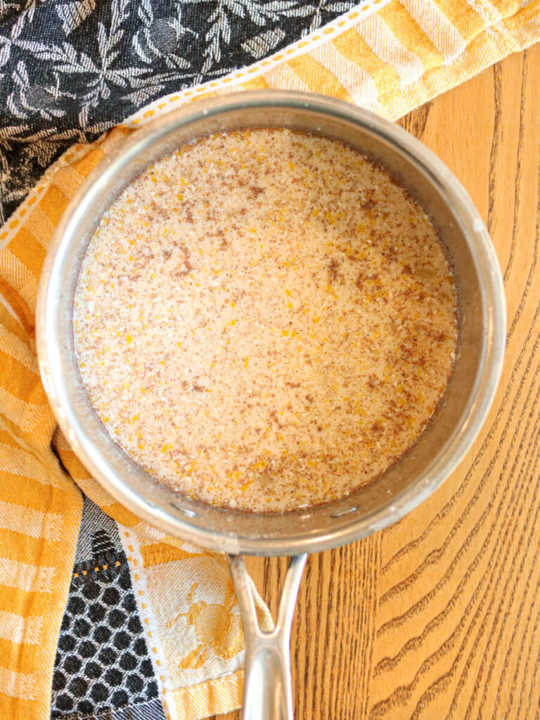 Milk, egg, syrup and spices whisked together in a saucepan on a wooden table.