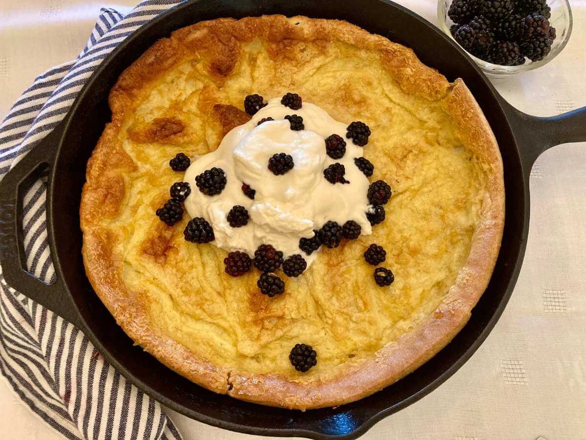 German pancake with whipped cream and blackberries in a skillet.