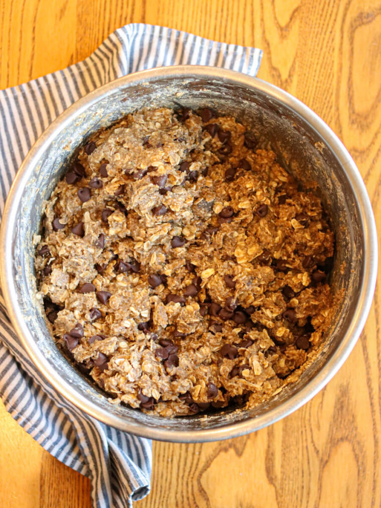Oatmeal chocolate chip cookie dough in a mixing bowl on a wood table.