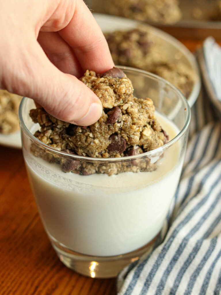 Person dipping oatmeal chocolate chip cooking into a glass of milk.