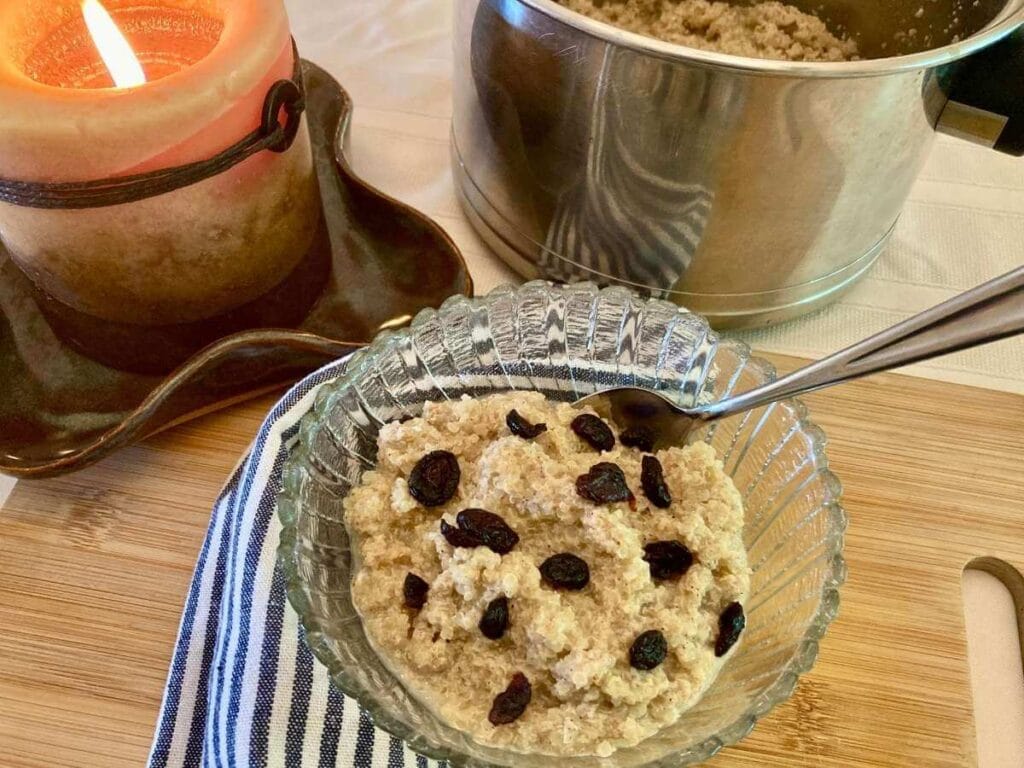 Quinoa pudding in a bowl with dried cranberries and a spoon and a pot of quinoa pudding.