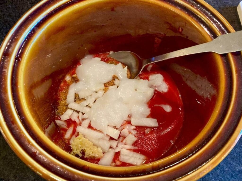 Stirring tomato sauce, chopped onions, and spices together in a slow cooker.