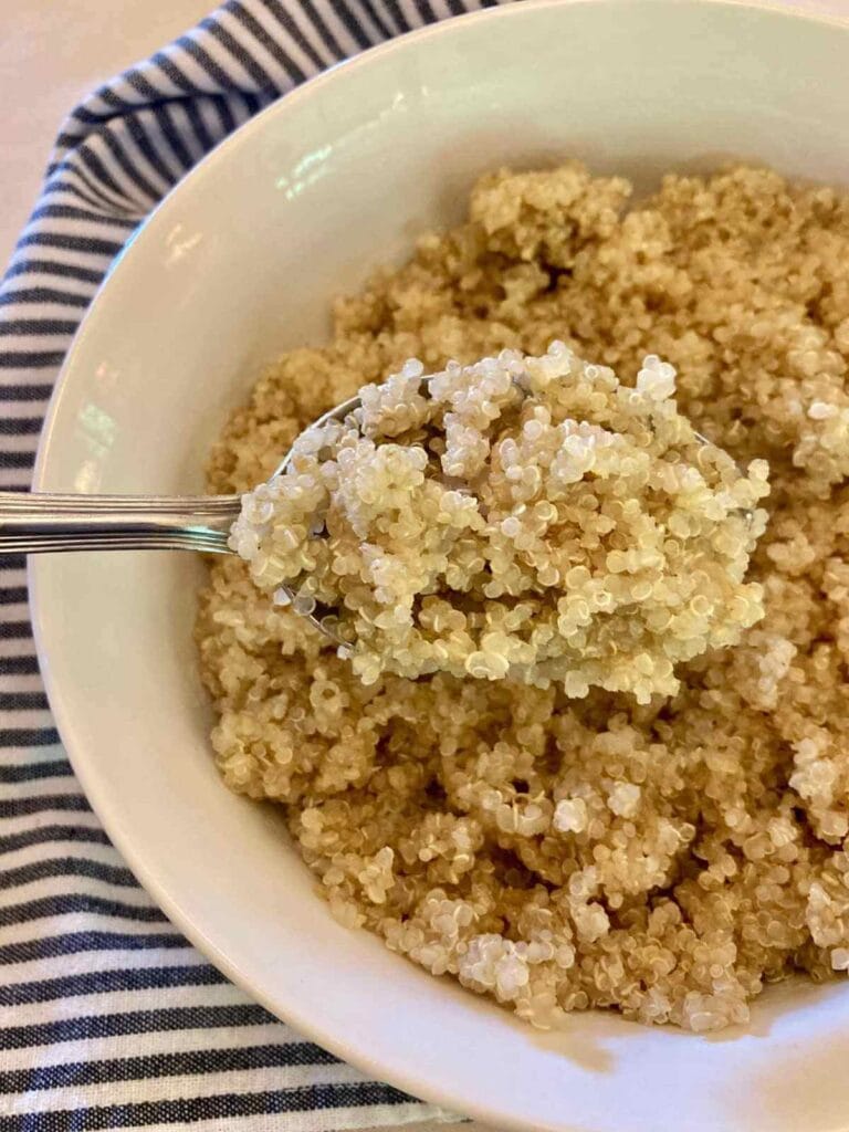 Spoon scooping cooked quinoa out of a bowl.