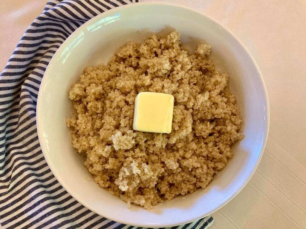 Bowl of cooked soaked quinoa with a slice of butter on top.