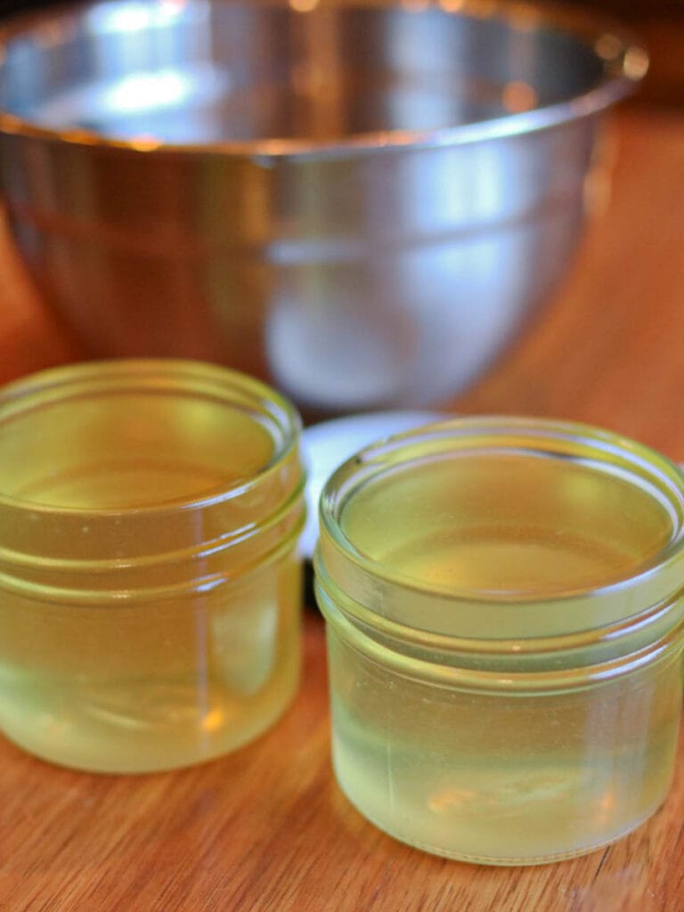 Melted tallow mixture cooling in two small glass jars on a wooden surface.