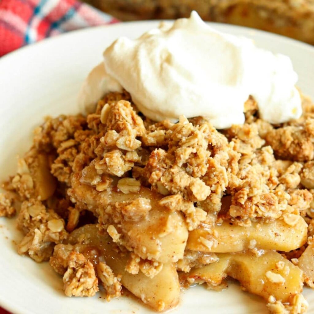 A closeup view of apple crisp topped with whipped cream on a plate ready to enjoy.