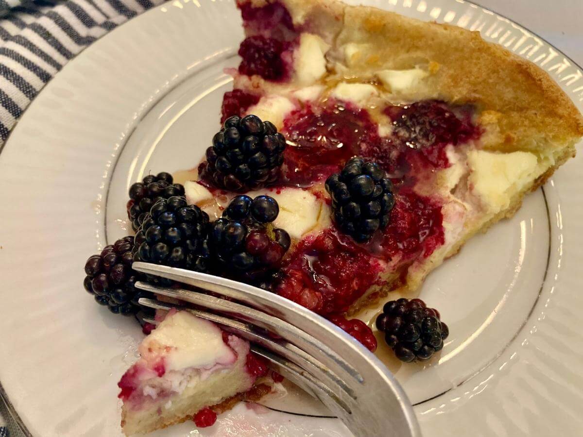 Slice of blackberry cheesecake German pancake on a plate with a fork in it.
