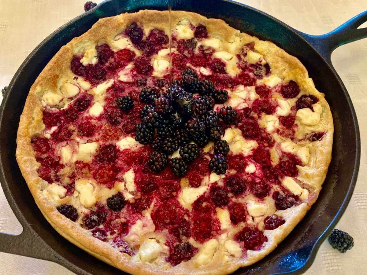 Skillet with blackberry cheesecake German pancake with blackberries on top.
