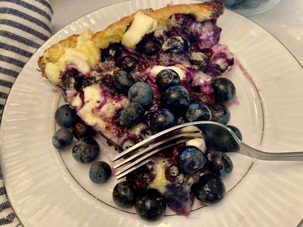 Slice of blueberry cheesecake German pancake on a plate with a fork in it.