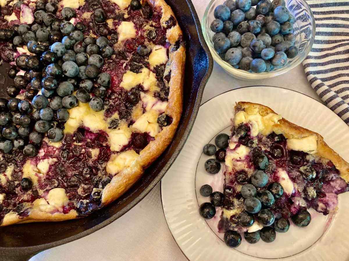 Slice of blueberry cheesecake German pancake with the rest of the pancake in a skillet.