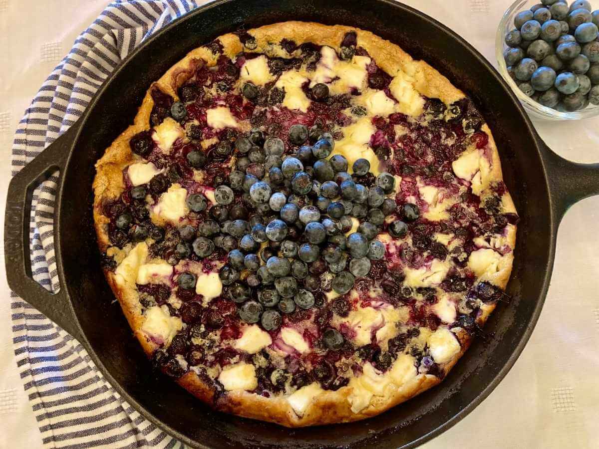 Top view of blueberry cheesecake German pancake in a skillet with fresh blueberries on top.