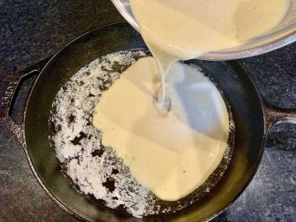 German pancake batter pouring into cast iron skillet.