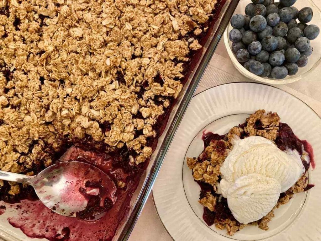 Gluten-free blueberry crisp on a plate beside pan of blueberry crisp.