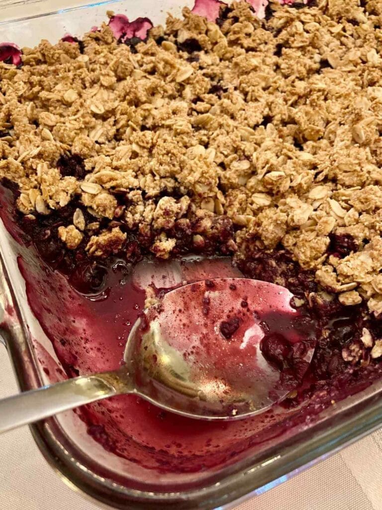 Scooping gluten-free blueberry crisp out of a pan.