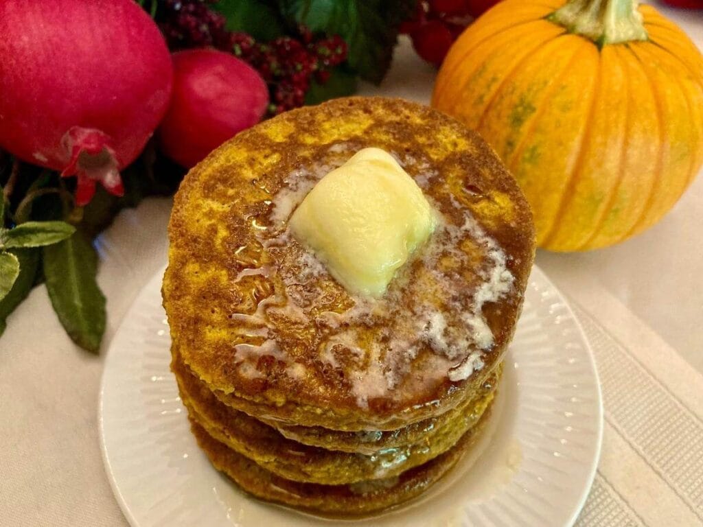 Stack of gluten-free pumpkin pancakes with butter on a plate.